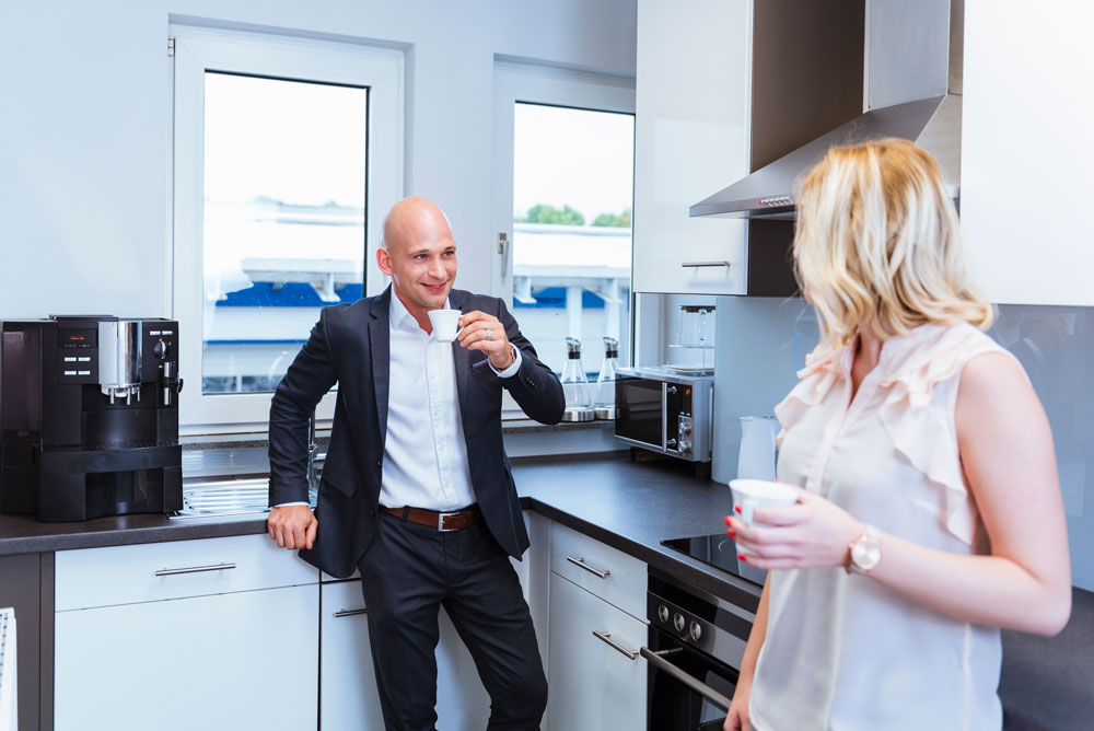 En man och en kvinna tar en kaffepaus i köket på ett kontor.